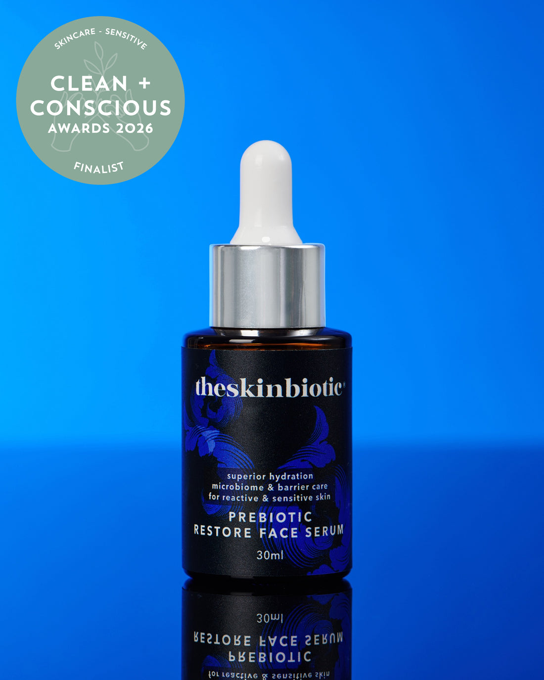 A bottle of theskinbiotie Prebiotic Restore Face Serum with a white dropper cap and silver collar, set against a vibrant blue gradient background. A green circular &